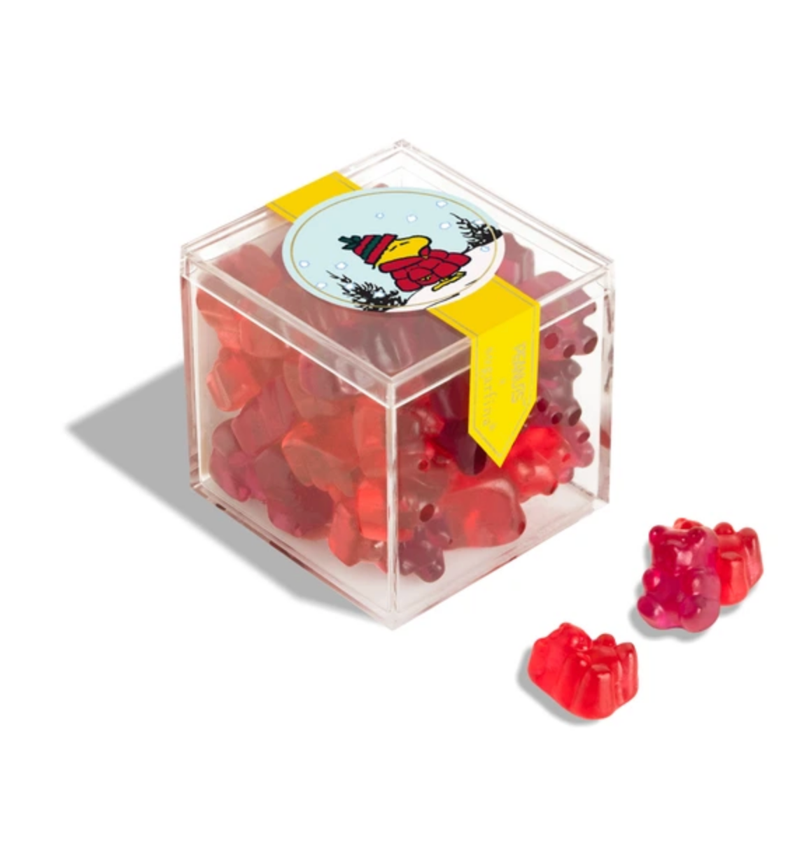 The Faire Christmas Candy Cube features red gummy bear-shaped holiday candies in a clear plastic box, finished with a yellow ribbon and a bear-in-winter-hat sticker—perfect for festive gifting or treating yourself.