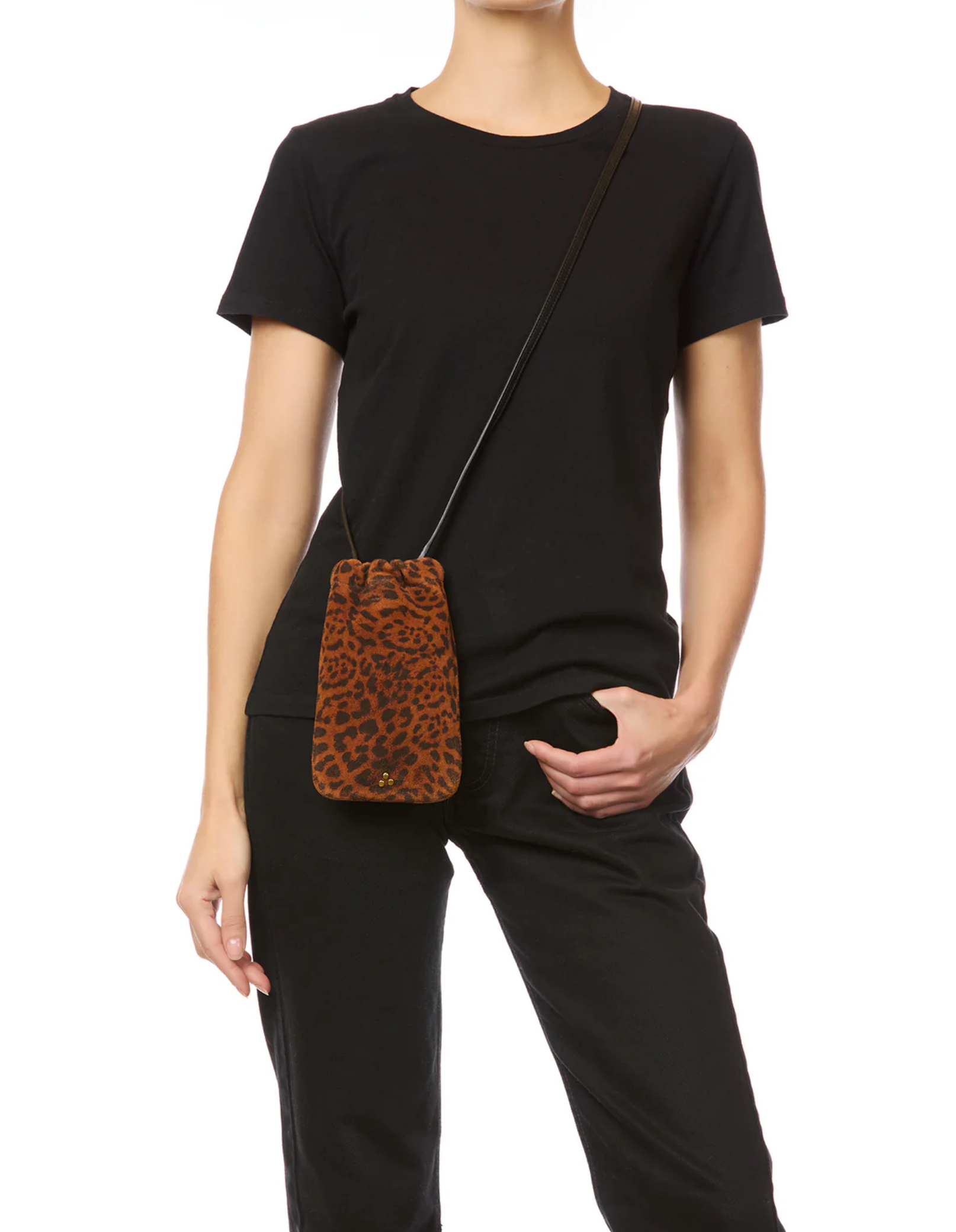 A person in a black t-shirt and pants stands with the Jerome Dreyfuss Gordi Mobile, a small brown leopard-print crossbody bag with leather shoulder strap, hanging from their shoulder against a white background.