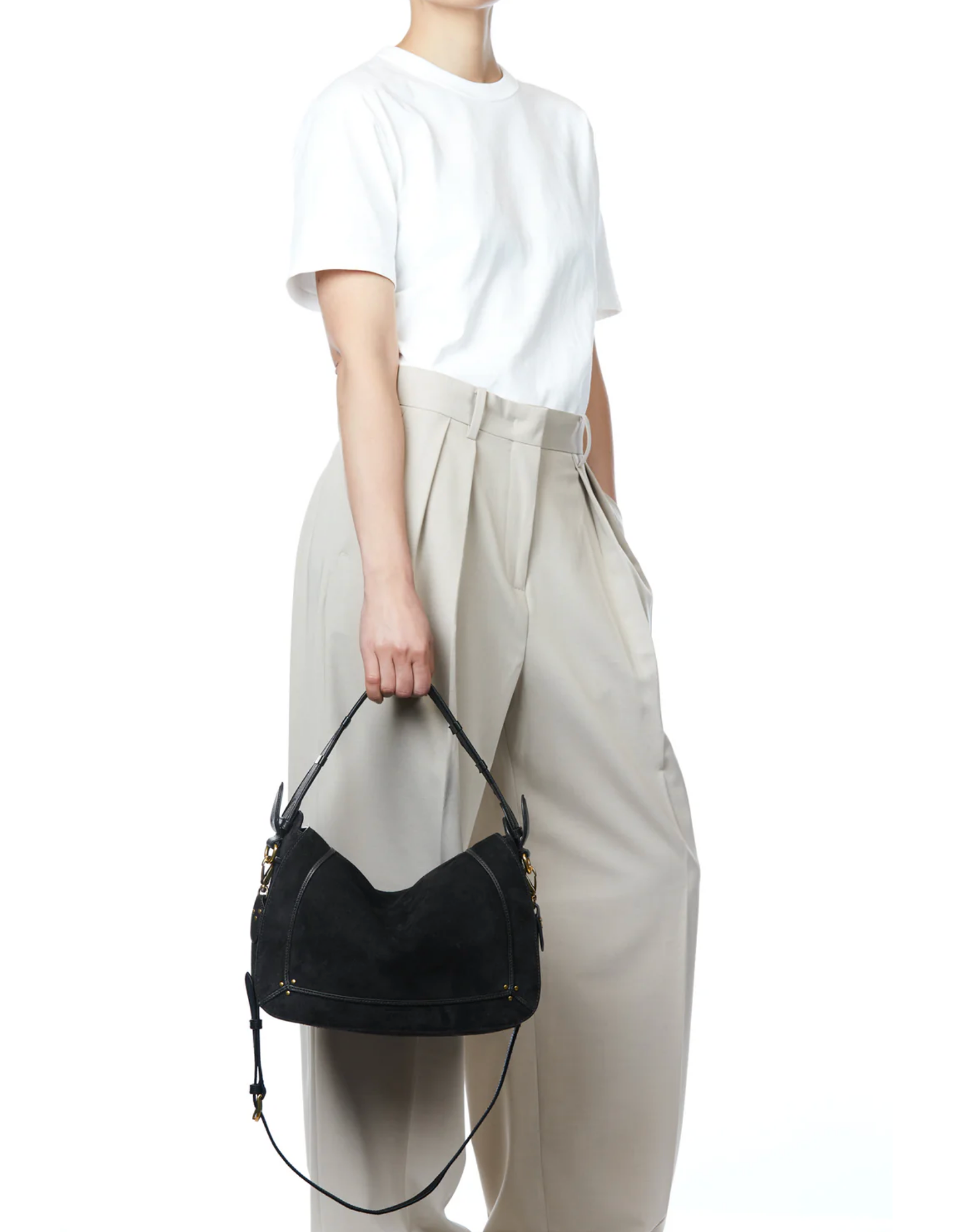 A person in a white T-shirt and high-waisted beige trousers stands with one hand in their pocket, holding the Jerome Dreyfuss Pepito Large Bag—a quilted leather handbag with gold hardware—against a white background.