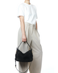 A person in a white T-shirt and high-waisted beige trousers stands with one hand in their pocket, holding the Jerome Dreyfuss Pepito Large Bag—a quilted leather handbag with gold hardware—against a white background.