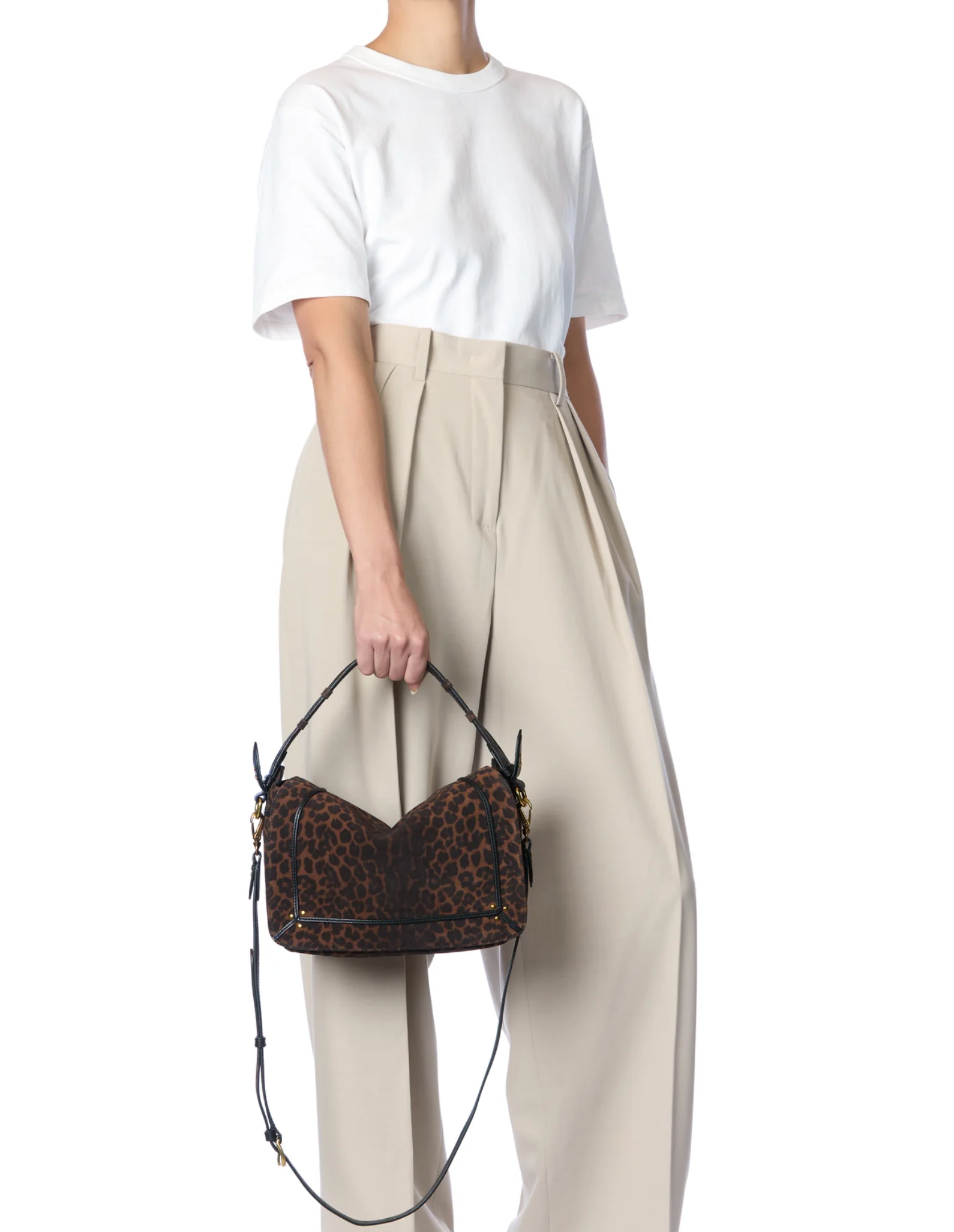 A person in a white t-shirt and high-waisted beige trousers holds the Pepito Medium Bag by Jerome Dreyfuss—a brown leopard print handbag with black straps. The image is cropped at the shoulders, so their face is not visible.