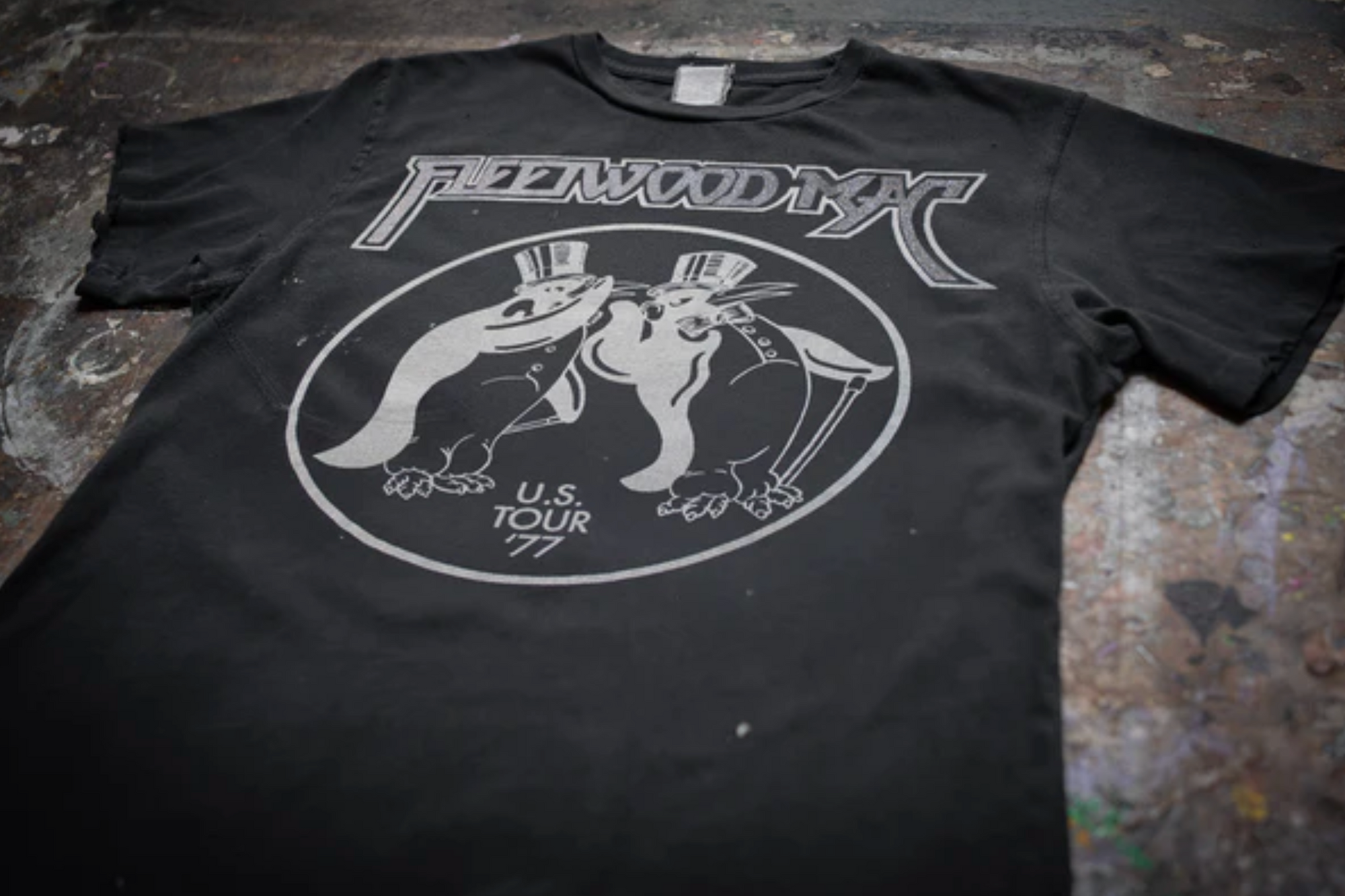 The Made Worn Fleetwood Mac Tee is a vintage unisex black shirt made in the USA, featuring two penguins in top hats, "Fleetwood Mac" above, and "U.S. Tour '77" below.