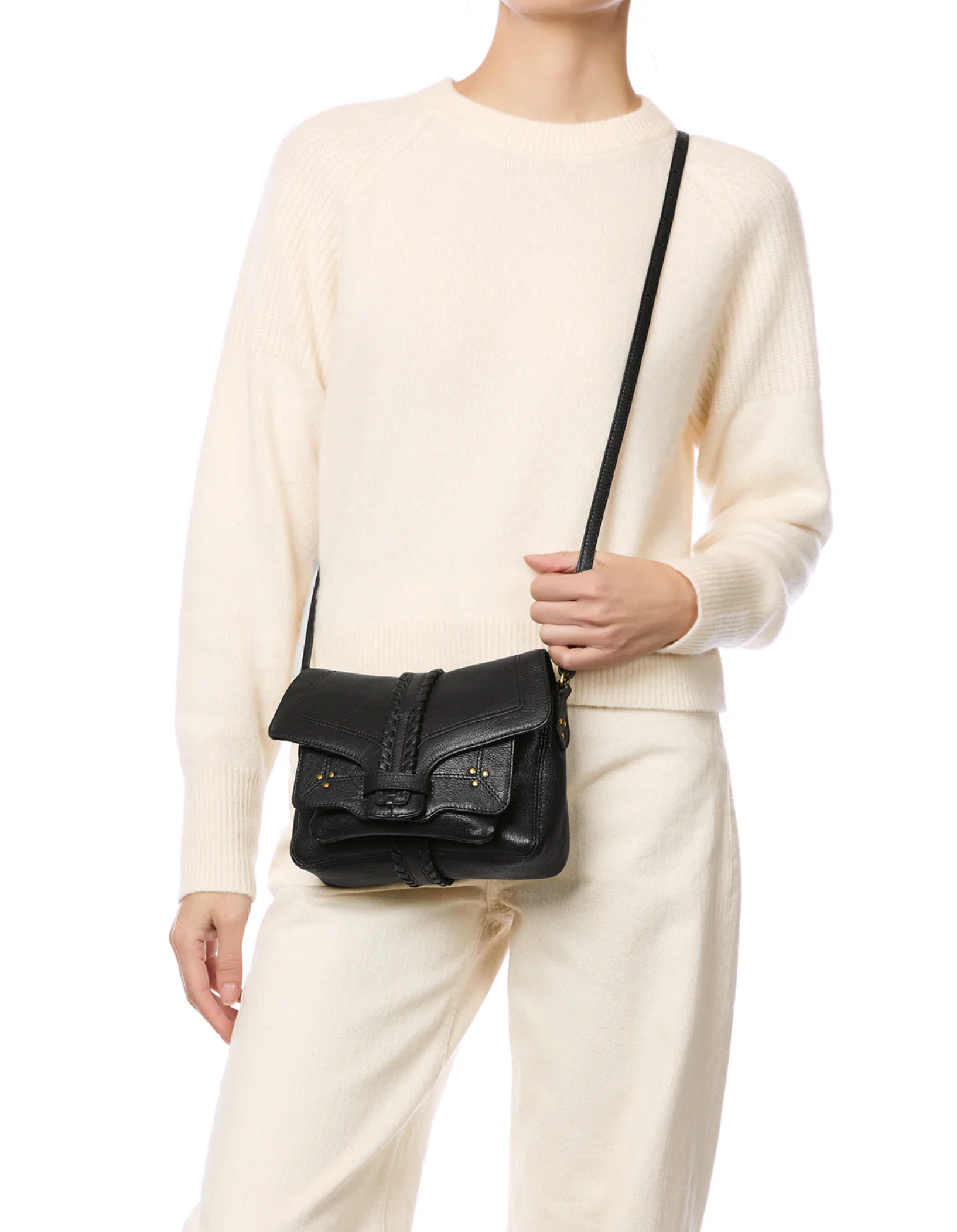 A person in a cream sweater and pants carries the Jerome Dreyfuss Harry Handbag—a black goatskin crossbody with a front flap and buckle detail. The image is cropped at the neck.