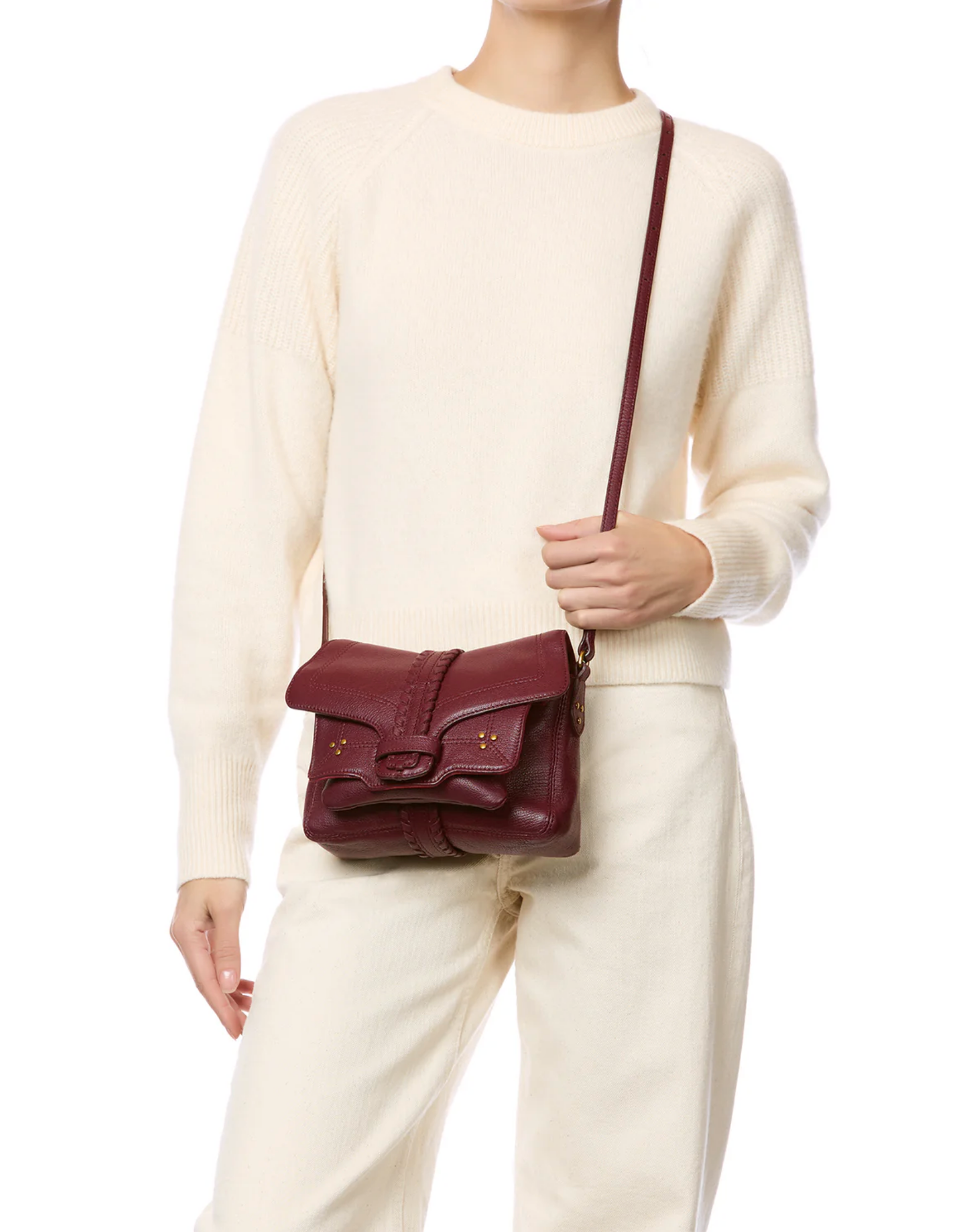 A person in an ivory sweater and matching pants holds the Jerome Dreyfuss Harry Handbag, a maroon goatskin crossbody with a flap closure and gold accents. The image is cropped at the shoulders and mid-thigh.