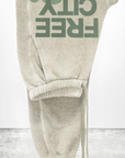 The FREECITY LARGE SUNFADES pocket sweatpant by Free City (sparrow, LLC) is a light beige unisex French terry pant shown upside down, with "FREE CITY" in large green letters and "freecity BASICgoodness" in black on the leg.