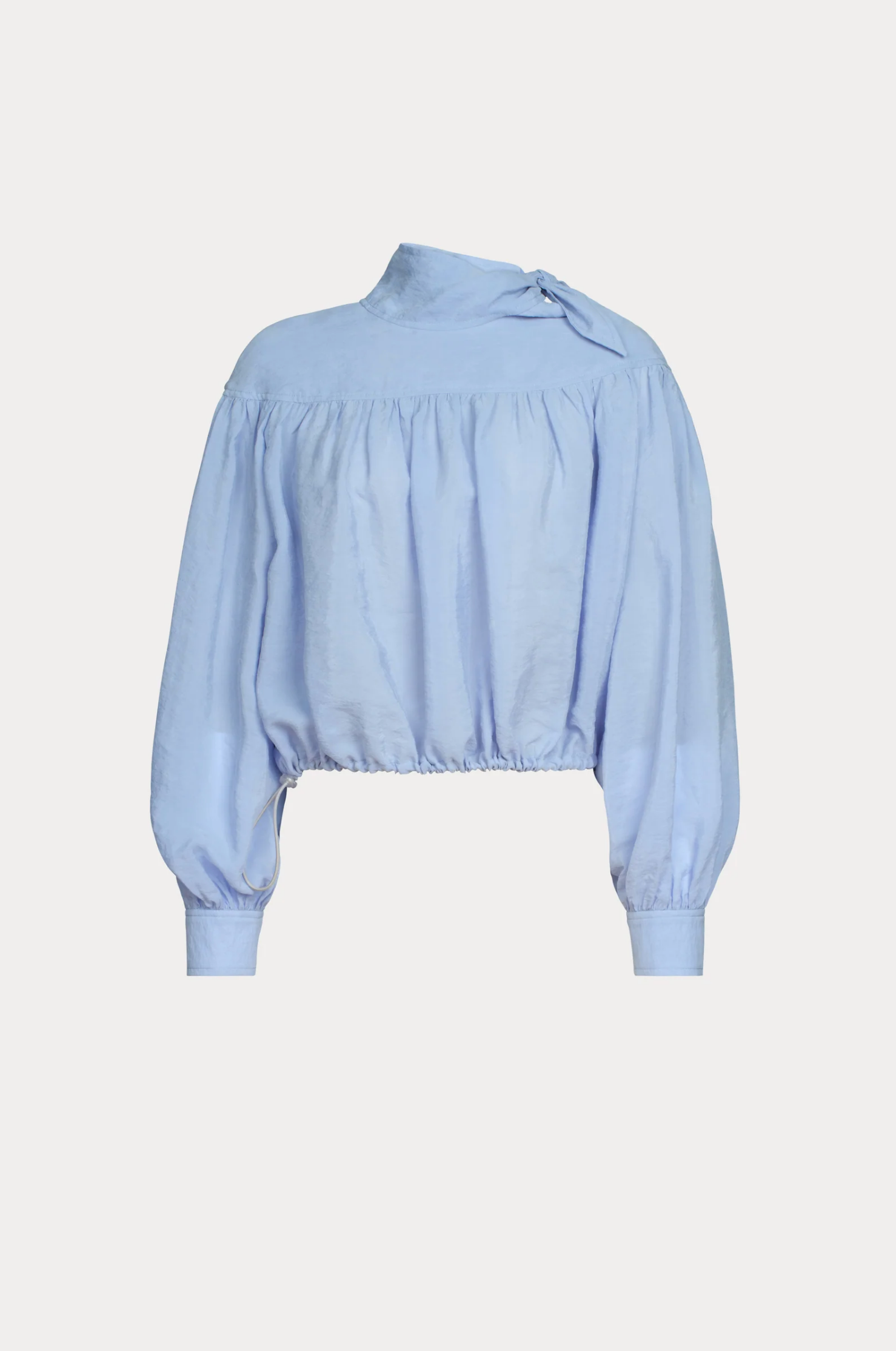 The Parachute Top by Rachel Comey is a light blue, wrinkle-resistant, long-sleeve blouse with a high neckline, gathered yoke, puffed sleeves, fitted cuffs, an asymmetrical neck bow, and an elasticized cropped hem—ideal for stylish travel.
