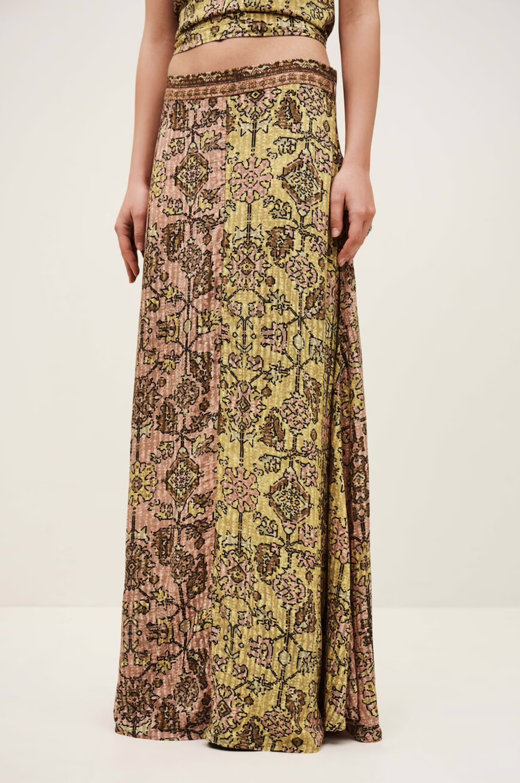A person wears the BA&SH Skirt Pario, a flared midi skirt featuring intricate vintage-inspired geometric and floral patterns in muted yellow, pink, and brown tones, standing against a plain light background.