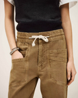 Wearing BA&SH Pant Fima—high waist brown drawstring pants with large front pockets—paired with a black sleeveless top over a white shirt and a silver bracelet, the person stands with one hand in their pocket.
