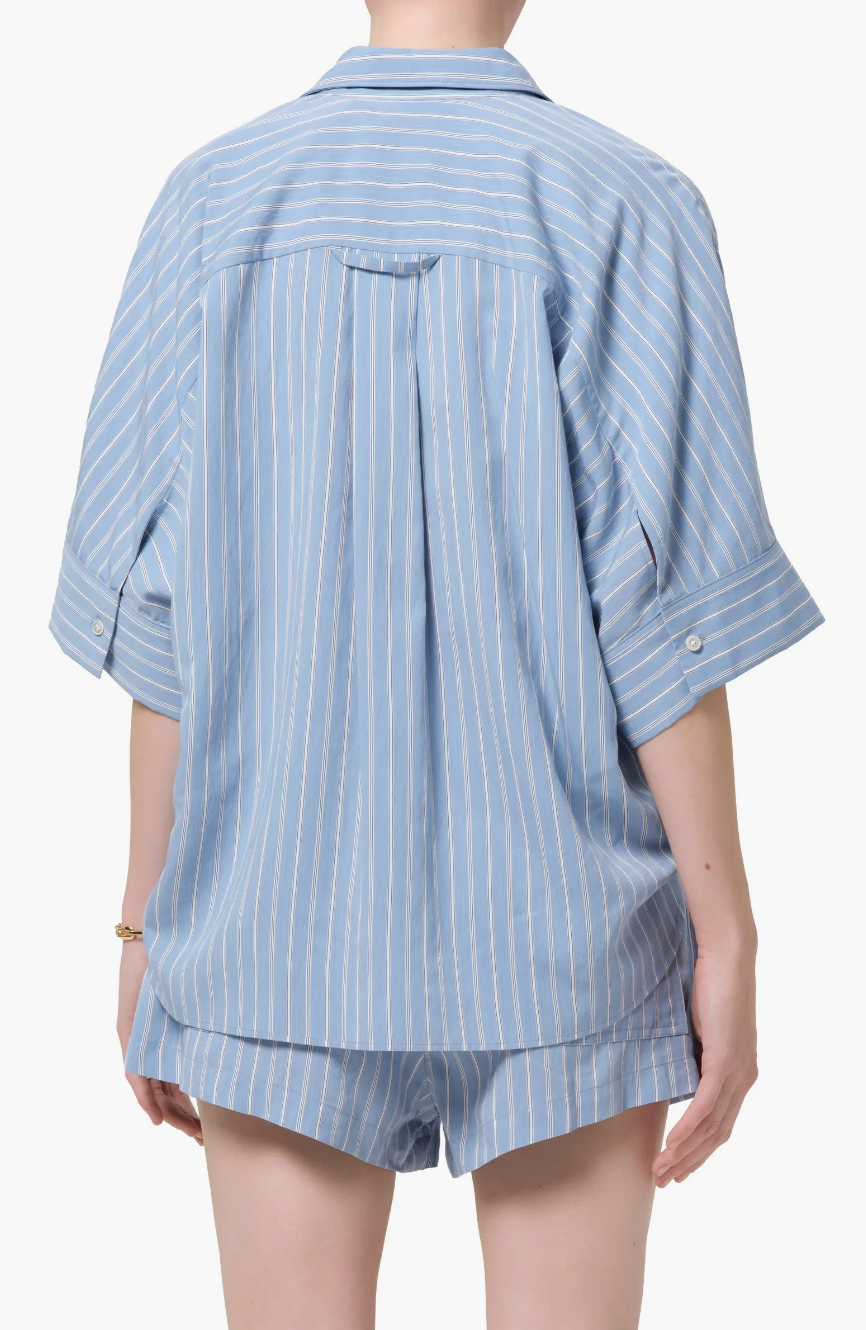 A person shown from the back in a Claire Origami Stripe short-sleeved, light blue button-up shirt with white vertical stripes and matching shorts by Citizens Of Humanity/AGOLDE, set against a white background.