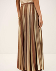 A person wearing the Rima Skirt by BA&SH—a 100% viscose maxi knit skirt with vertical brown, beige, and tan stripes—pairs it with a sleeveless beige top, standing against a plain light background.