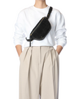 Jerome Dreyfuss Lino Banane black calfskin crossbody bag styled with a white sweatshirt and beige pleated pants.