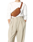 Jerome Dreyfuss Lino Banane bag styled with a white sweater and beige pleated pants, hands in pockets.