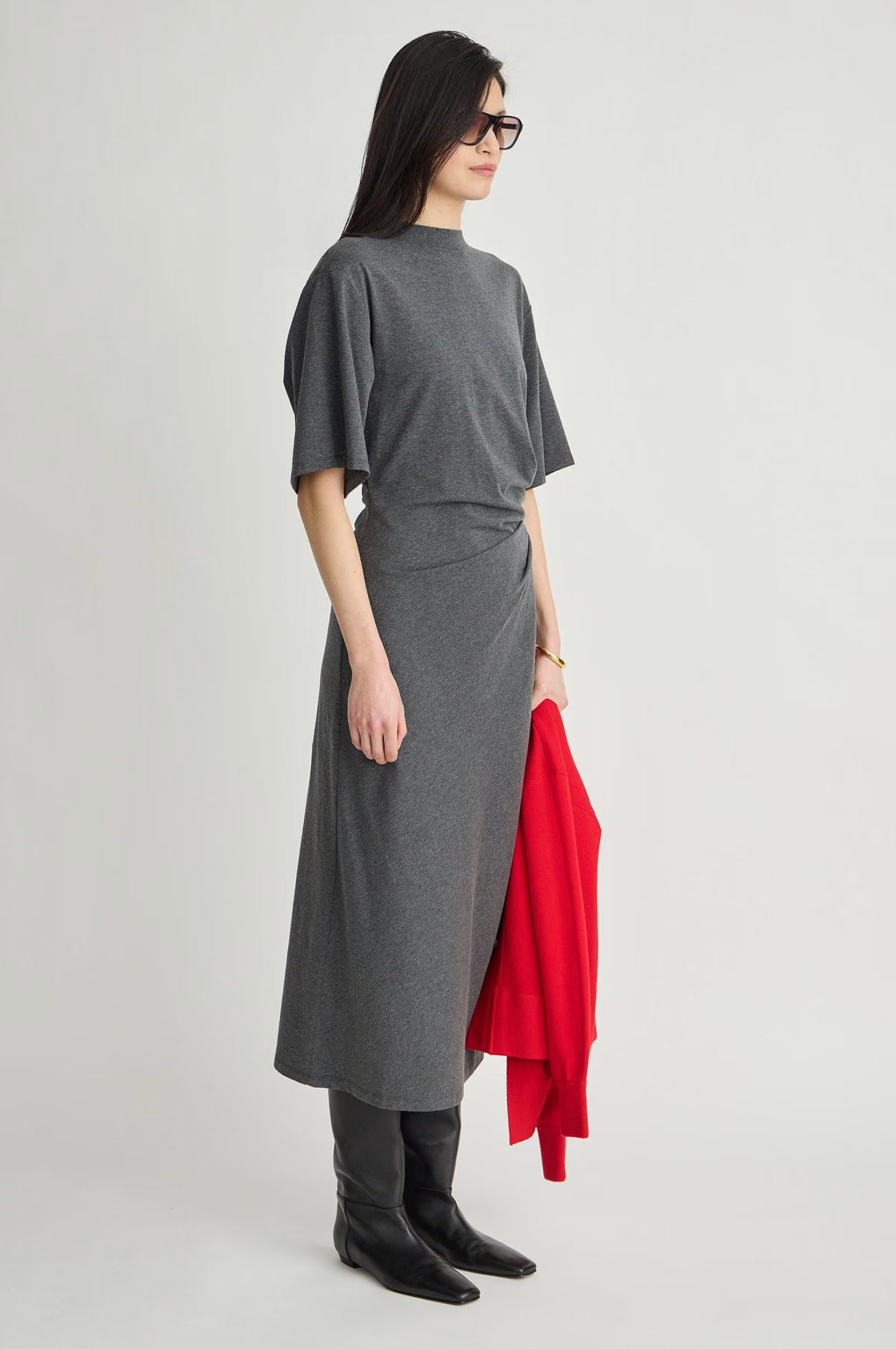Luna Cinched Maxi dress by Apiece Apart styled with black boots, shown holding a red sweater against a plain backdrop.
