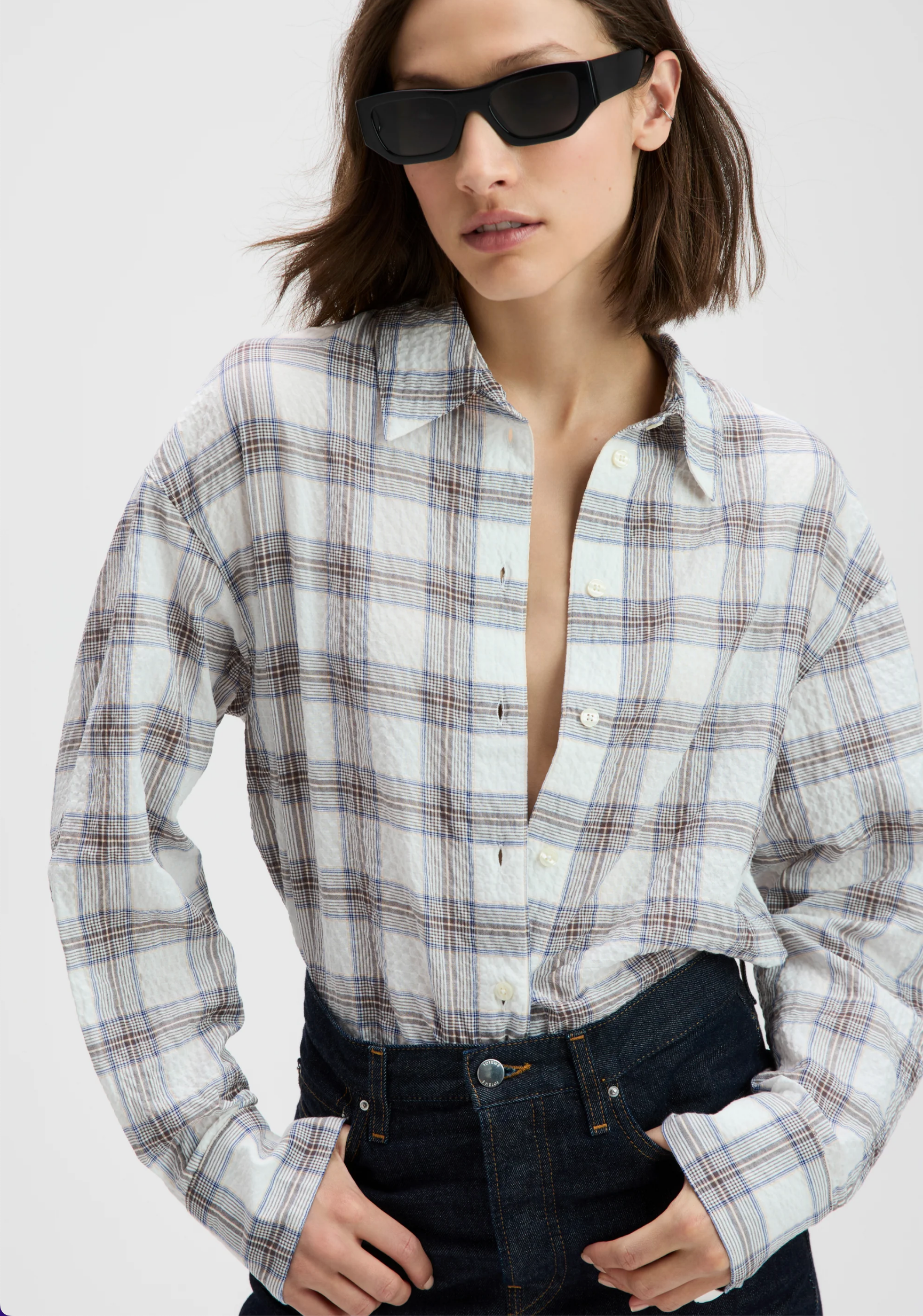 The Everything Shirt by Sold Out NYC, white and half unbuttoned, styled with dark high-waisted jeans and sunglasses.