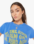 A woman wearing a blue T-shirt with the Boxy Goodie Goodie On The Road Again printed in yellow. She has a necklace and her brown hair is styled back Arizona-style.