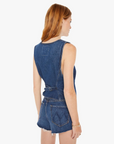 A woman with red hair wearing a sleeveless denim romper with a belted waist, viewed from the back. The outfit features a frayed hem and a patch pocket on the upper back, perfect for an Arizona style day by Mother's The Masked Rider.