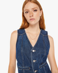 A young woman with red hair and freckles wearing a sleeveless denim dress with large buttons, standing against a plain white background. She has a subtle expression and wears a delicate necklace, perfectly embodying Mother style.