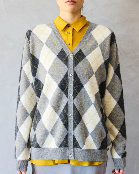 A person wears a yellow collared shirt under a gray, white, and black Brazeau Tricot Argyle Cardigan, standing against a light gray background. Only the upper body is visible.