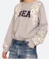 A person wears the Sea New York Georgie Sweatshirt—a light gray, true to size cotton blend with "SEA" in bold black letters, white floral embroidery and sequins—paired with distressed blue denim jeans.