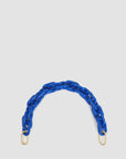 The "Shortie Strap" by Clare Vivier features a short handle of chunky, interlocked bright blue resin chain links with gold clasps at each end, set against a plain white background. It's perfect for adding a pop of color and style to any bag.