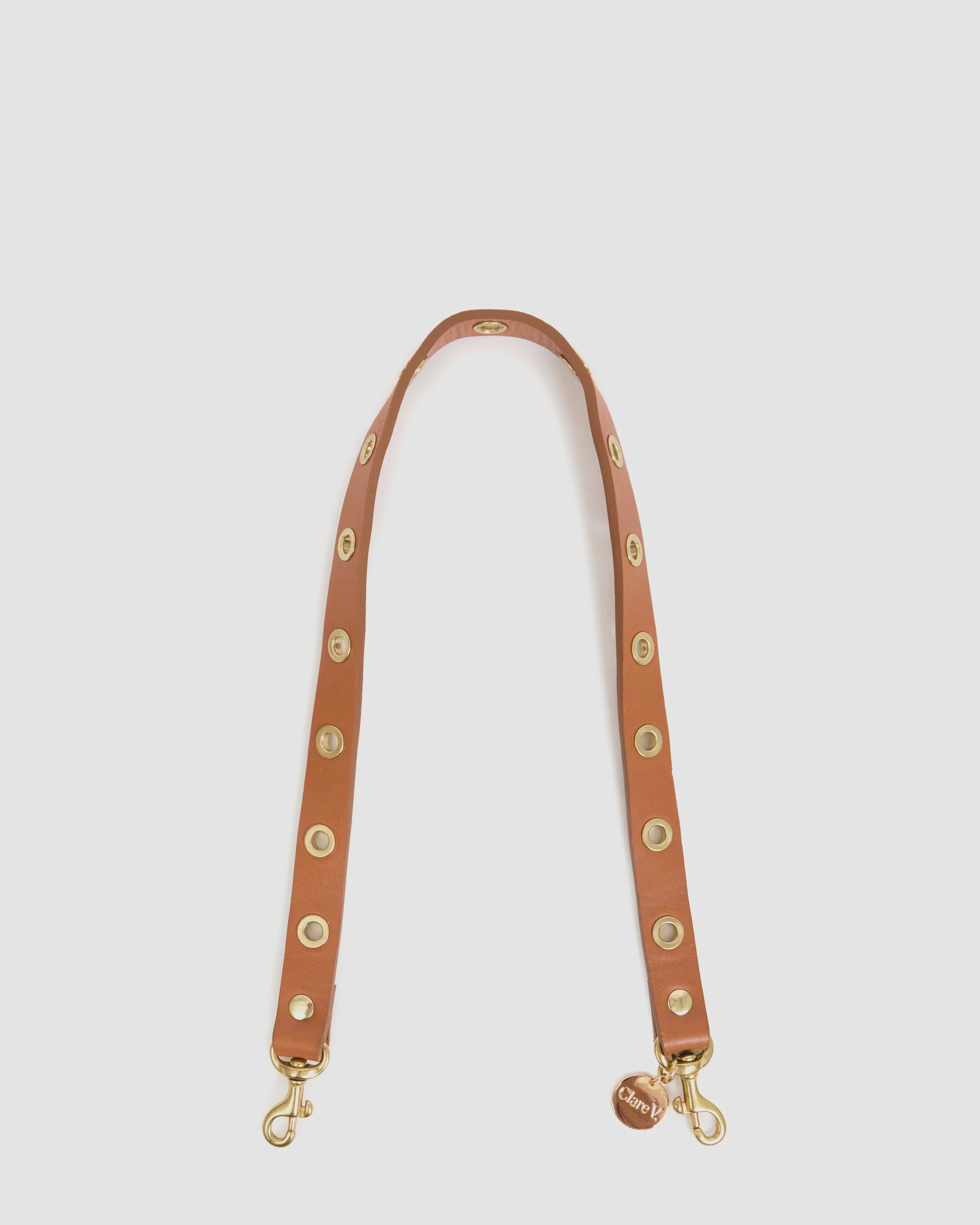 The Clare Vivier Shoulder Strap w/Grommets is a tan Italian leather bag strap with large brass grommets, gold clasps at each end, and a small round Clare Vivier tag near one clasp.