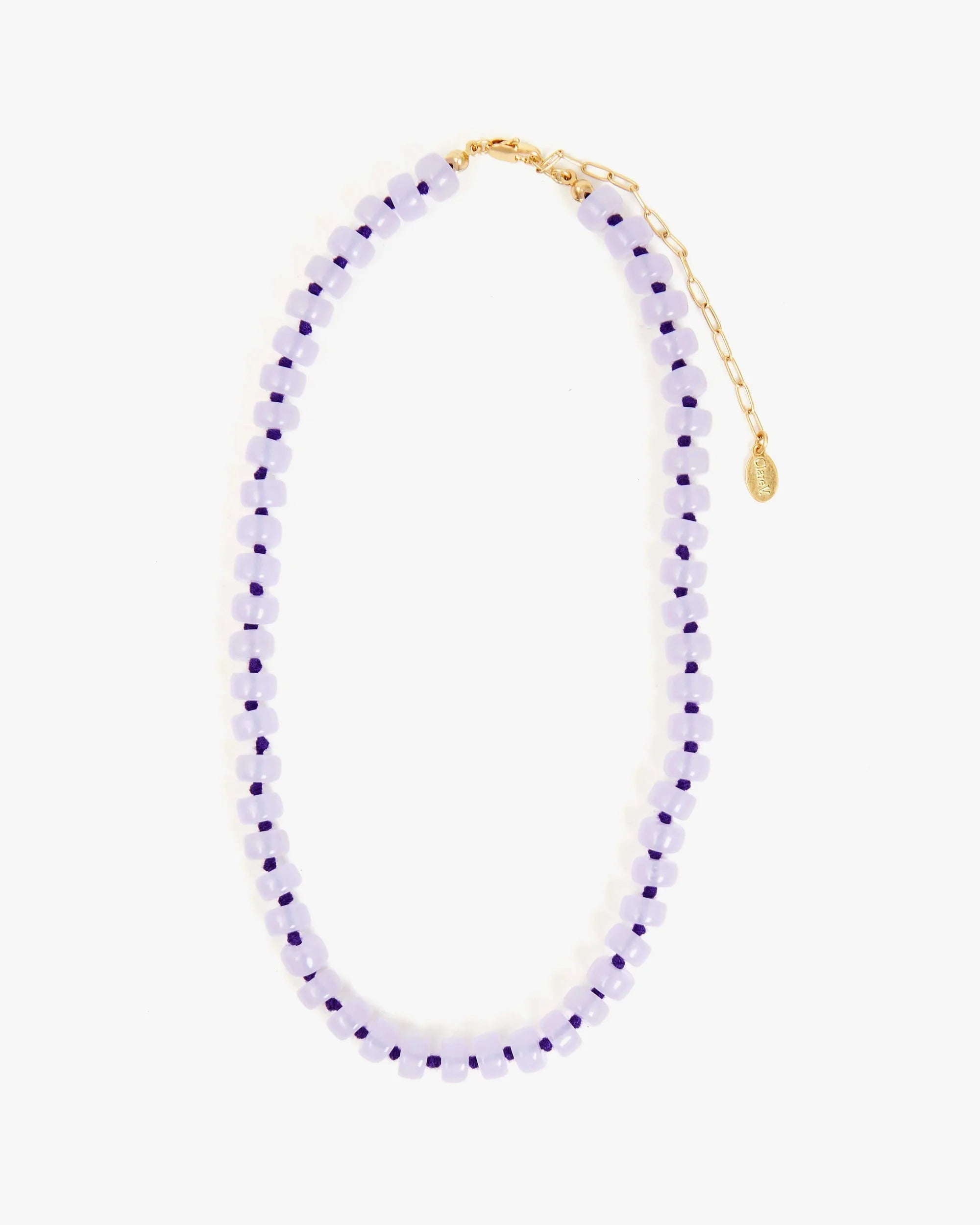 The Clare Vivier Stone Slice Necklace features alternating light and dark purple beads, transparent glass accents, a gold clasp, extender chain with small oval tag, and is displayed in a loose oval on a white background.