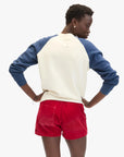 A person stands with hands on hips, wearing the Clare Vivier Sweatshirt F25—cozy cotton fleece with blue sleeves—and red shorts, seen from behind against a plain white background.