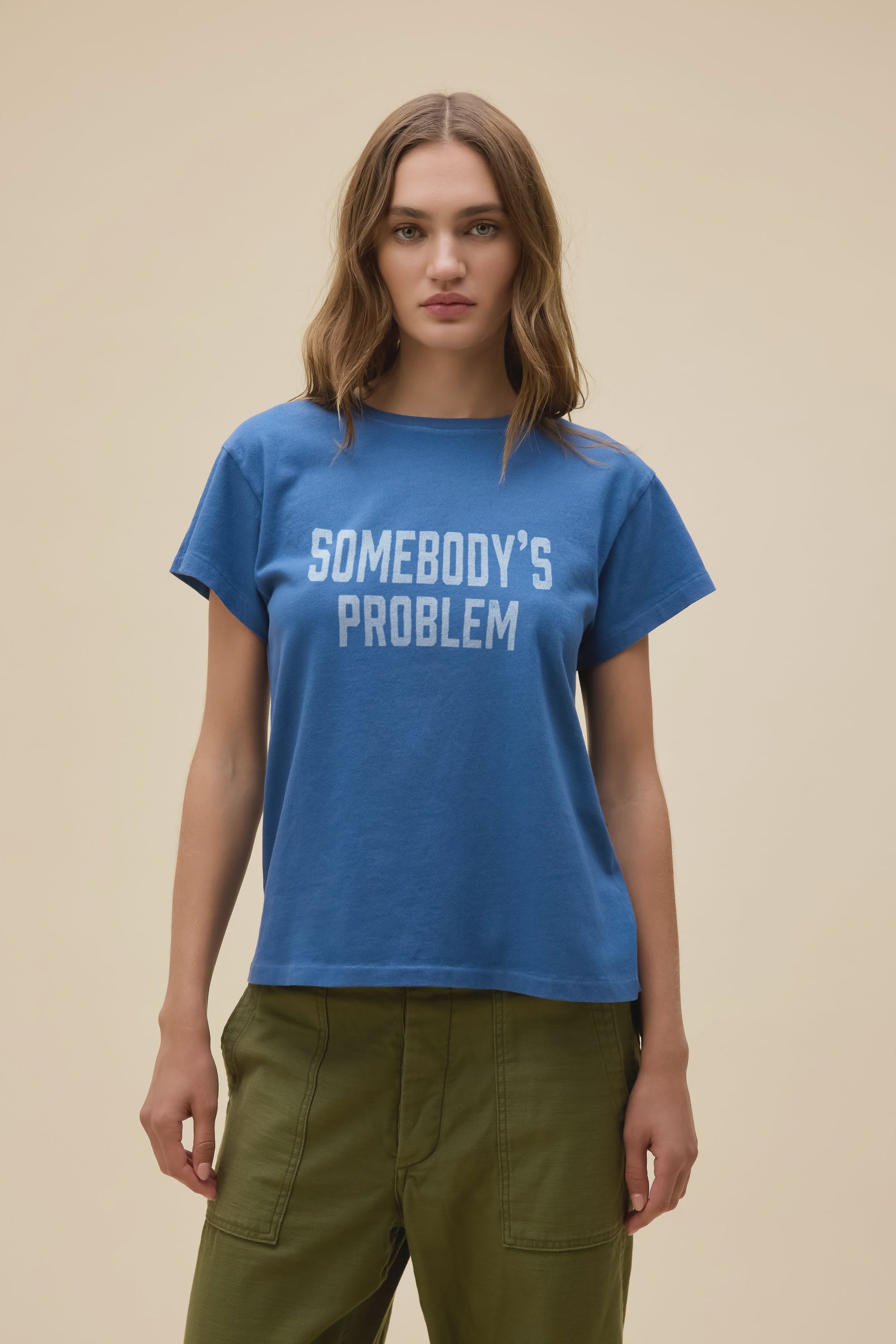 A woman with long, light brown hair wears the DayDreamer Morgan Wallen Somebodies Problem blue tee and olive green pants, standing against a plain beige background.