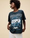 A woman with curly hair and white pants wears an oversized DayDreamer Backstreet Boys Into The Millennium tee, featuring band graphics, a globe, and blue stars, standing against a plain beige background.