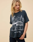 A blonde woman wears the DayDreamer "Morgan Wallen Ain't That Some" oversized cotton t-shirt, which features a pickup truck, trees, mountains, and the text "Morgan Wallen Ain't That Some." She gazes downward with one hand at her side.