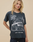 A blonde woman models the DayDreamer Morgan Wallen Ain't That Some oversized cotton T-shirt, which features a truck, trees, and the phrase "Ain't That Some." She stands against a plain beige background, looking slightly to the side.