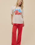 A person wears the DayDreamer Chicago Skyline Tee, featuring a blue skyline graphic and red "Chicago" text, paired with loose red pants and black shoes, standing against a plain beige background.