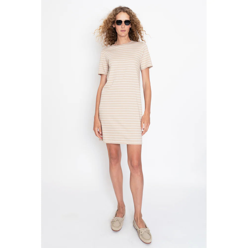 A curly-haired person in sunglasses wears Kule's The Tee Dress Sand/White Pinstripe, a short-sleeved, 100% cotton piece. They're also wearing light-colored loafers and standing against a white background.