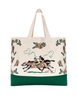The Derby Tote by The Great Inc. is a cotton canvas bag with green trim, two off-white handles, and a design of two jockeys on horses among colorful florals, inspired by American Western memorabilia.