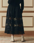 A person stands facing a beige paneled wall, wearing The Rosette Crochet Canary Skirt by The Great Inc., styled with light socks and cream shoes. Only the lower half of their body is visible.