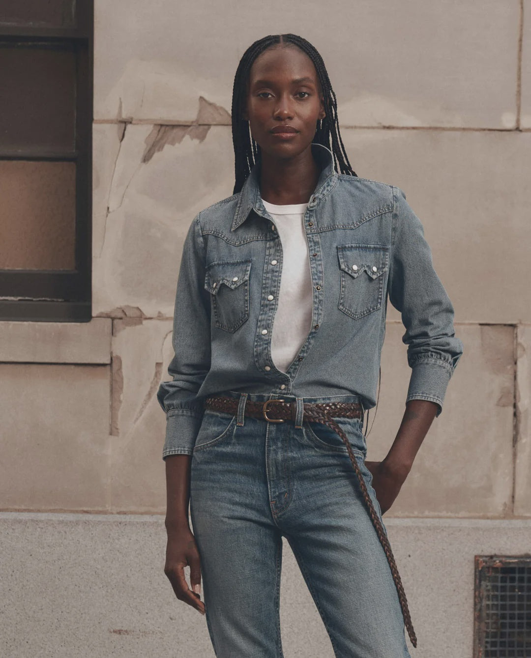 The Great Inc. Howdy Top in denim, styled casually with jeans, set against a rustic beige wall for a relaxed look.