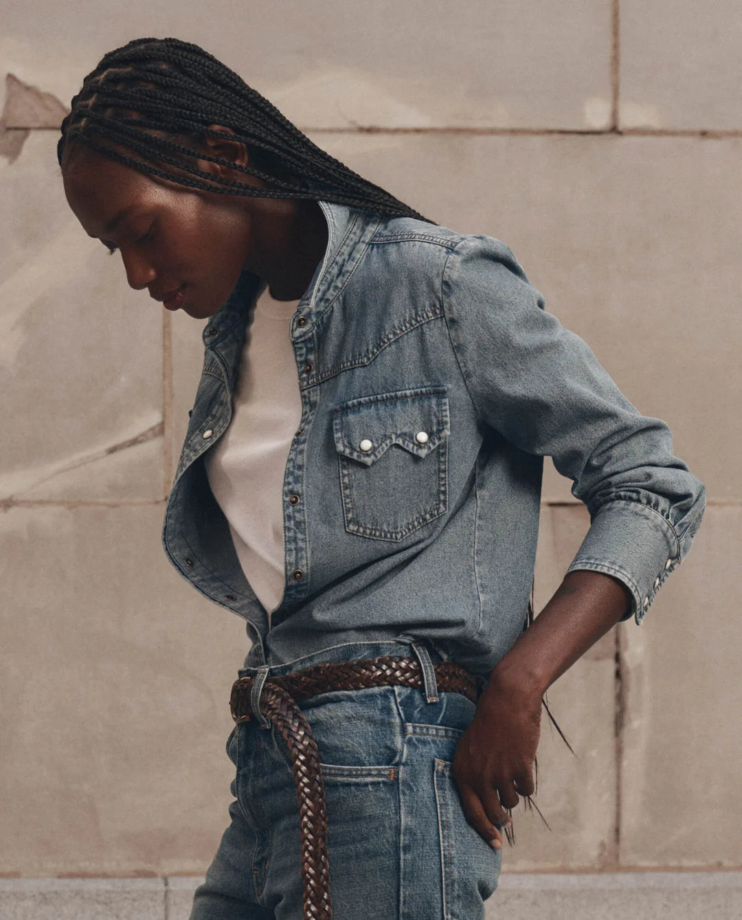 The Great Inc. Howdy Top lightweight denim shirt with pearl snaps, styled casually with jeans against a neutral wall.