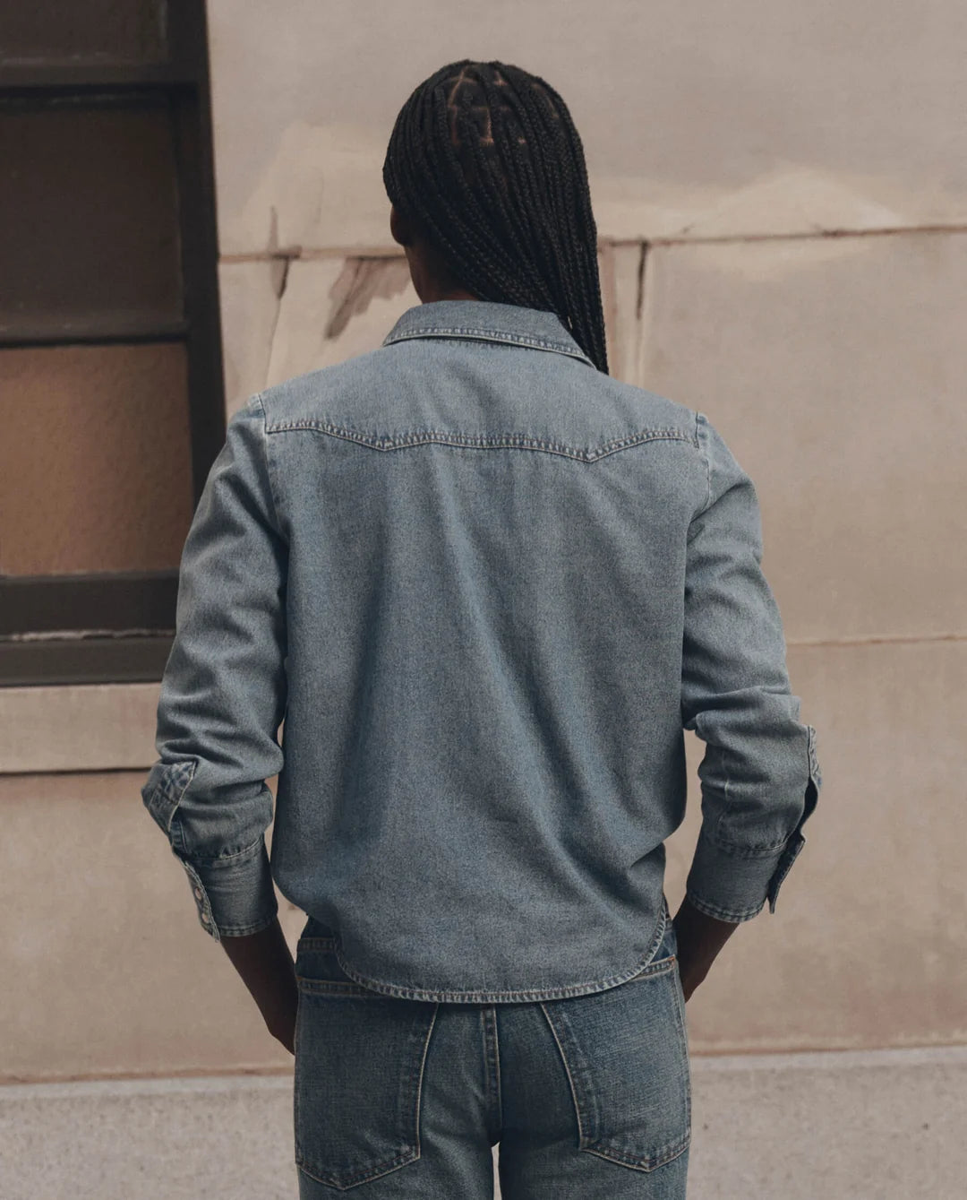 Lightweight denim Howdy Top by The Great Inc. with pearl snaps, seen from the back on a person with long braids.