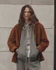 Brown fleece hoodie from The Great Inc. styled casually with sweatpants near a stone wall, relaxed lifestyle setting.