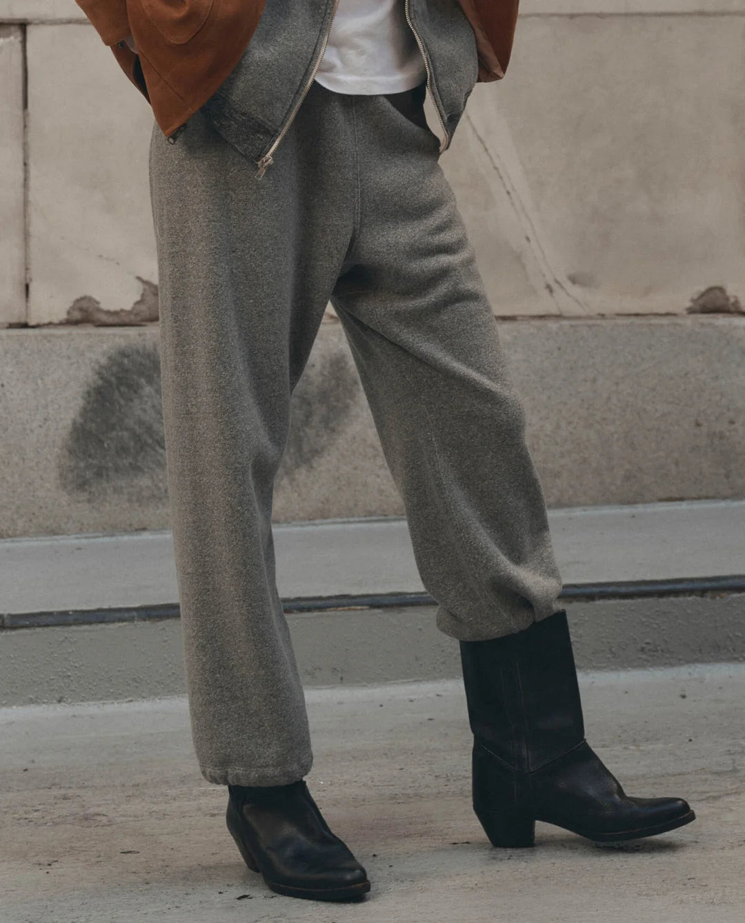 The Great Inc. Fleece Sport Sweatpant in a casual street style, paired with black boots and a brown jacket on sidewalk.