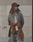 The Great Inc. Fleece Campus Hoodie in red, styled with a cap, worn casually by a textured concrete wall.