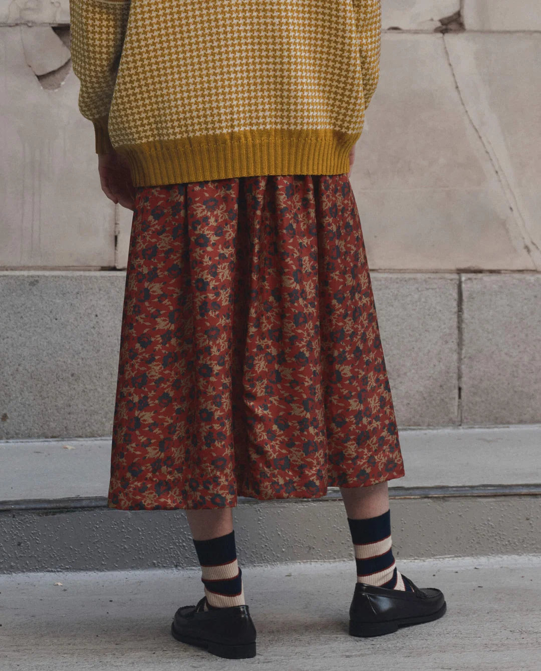 Yellow The Canary Skirt by The Great Inc. styled with a matching sweater and striped socks on concrete.