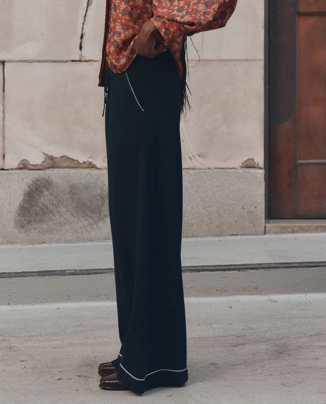 Menswear Tipping Trouser by The Great Inc. in a relaxed stone and wood setting with patterned shirt styling.