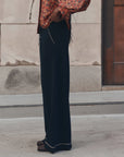 Menswear Tipping Trouser by The Great Inc. in a relaxed stone and wood setting with patterned shirt styling.