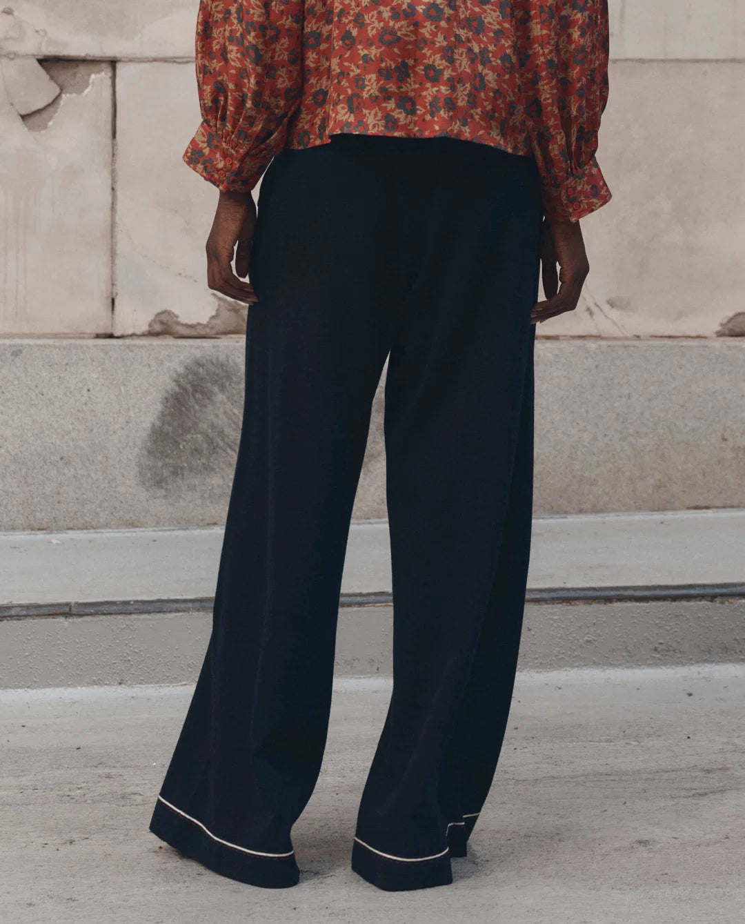 The Great Inc. Menswear Tipping Trouser with a red floral blouse, styled outdoors on a concrete patio.