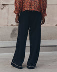 The Great Inc. Menswear Tipping Trouser with a red floral blouse, styled outdoors on a concrete patio.