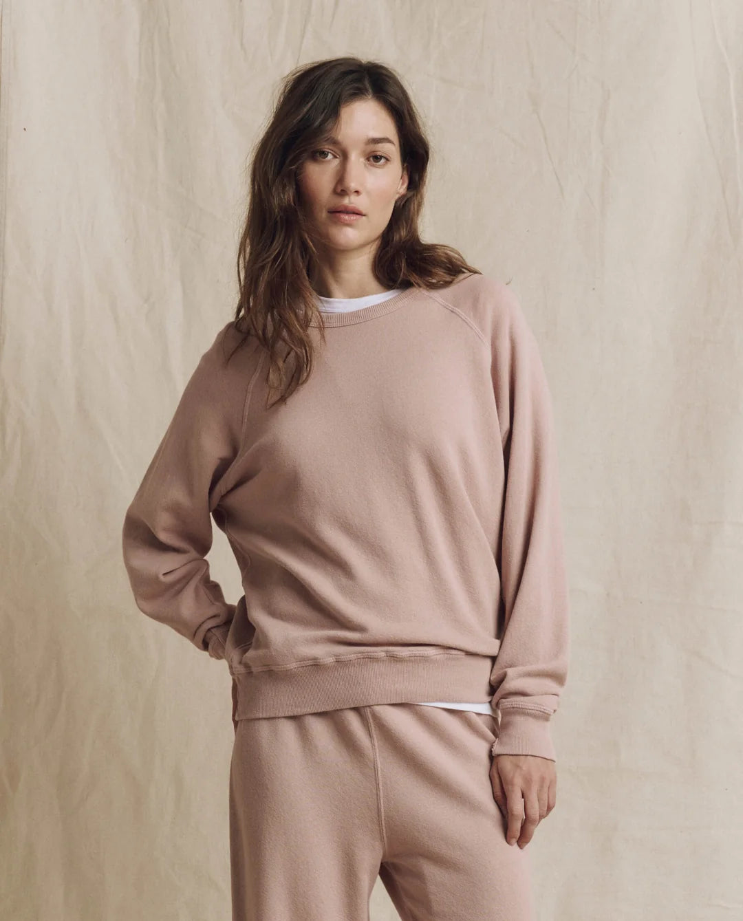 The Great Inc. College Sweatshirt 2026 in soft beige, casual fit, styled against a fabric backdrop.