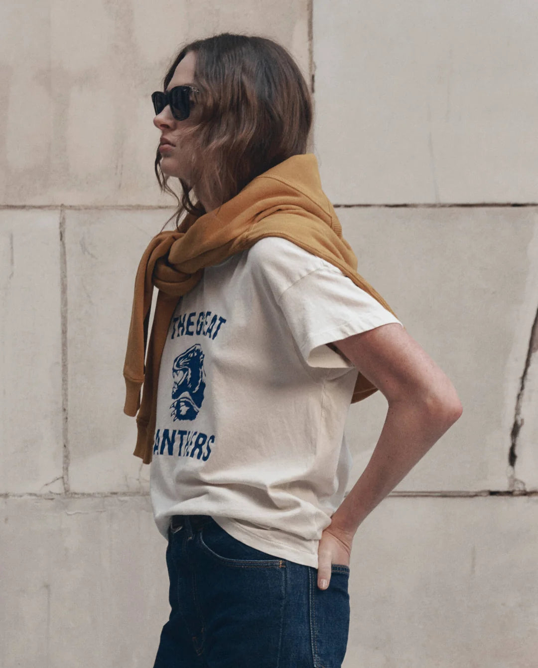 Boxy Crew Growling Panther tee by The Great Inc. styled with dark jeans and mustard sweatshirt by a stone wall.