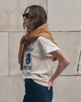 Boxy Crew Growling Panther tee by The Great Inc. styled with dark jeans and mustard sweatshirt by a stone wall.