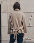 The Commander Riding Cardi by The Great Inc., leather knot buttons, tied belt, modeled near a stone wall.